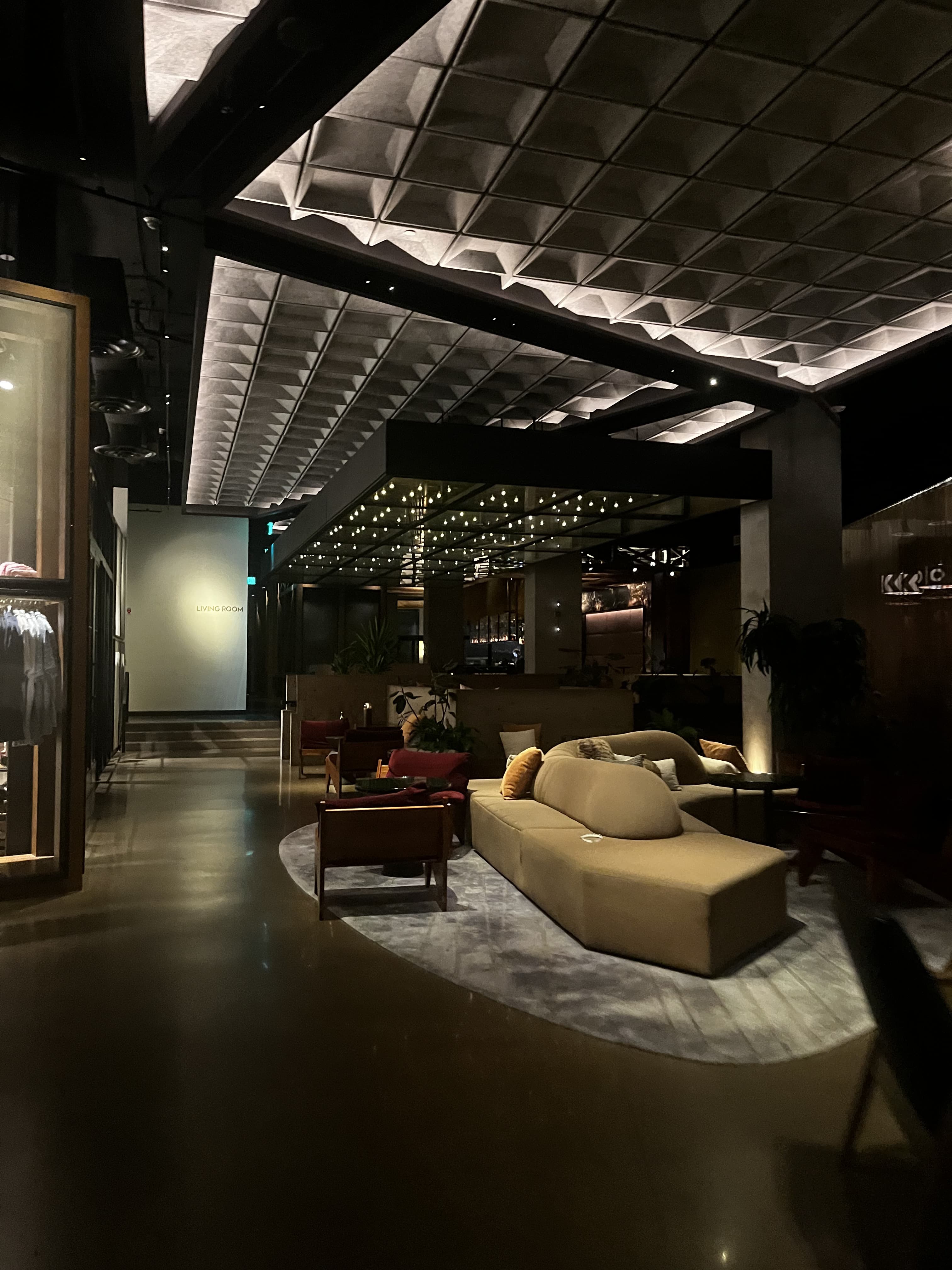 Dimly lit modern lounge with a geometric coffered ceiling, tan sectional sofa, and armchairs.